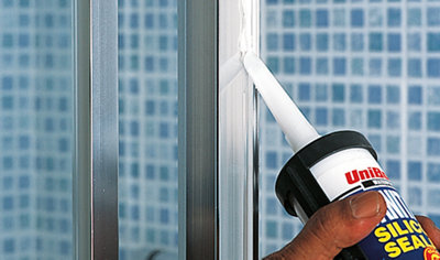 Running a bead of silicone sealant along the wall channel of a shower enclosure.