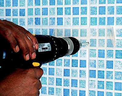 Person using a drill to drill a hole in a tiled bathroom wall.