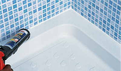 Using a sealant gun to run a bead of silicone sealant around the edge of a shower tray where it meets a tiled wall.
