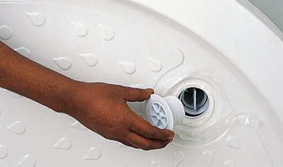 Person fitting a waste outlet to the hole in a shower tray which has a bead of silicone around the edge.