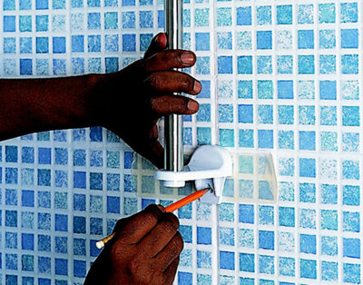 Person marking the fixing holes for a shower rail bracket on bathroom tiles with a pencil.