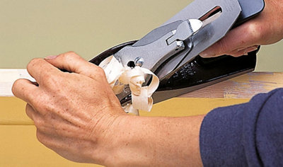 A person using both hands to run a planer along the edge of an internal door, removing enough wood to prevent the door from sticking.