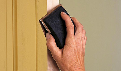 A person using a piece of sandpaper to smooth the edge of an internal door that has just been planed.