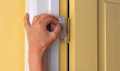 A person placing a small piece of cardboard, folded in half, behind the hinge of an internal door to pack out the space behind the hinge.