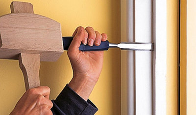 A person using a wooden mallet to strike a chisel, levering the doorstop of an internal door away from the door frame.