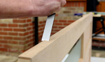A person using a chisel to cut a recess in a timber door, preparing it for the installation of hinges.