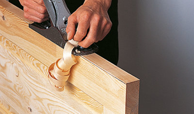 A person running a plane along the top of a wooden door to trim small amounts off the edges.