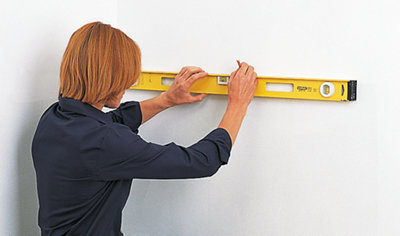 A person holding a spirit level firmly against a wall with one hand while using a pencil in the other hand to make a precise marking on the wall.