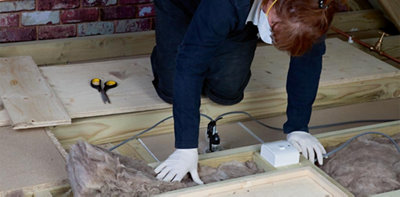Person wearing gloves and a dust mask pushing loft insulation between the gap between two joists in a loft.