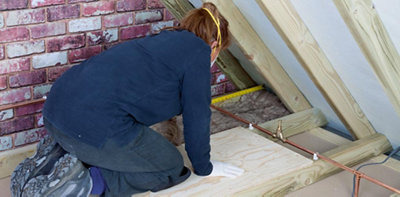 Person in a loft wearing gloves and a dust mask rolling out insulation between two joists.