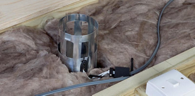 Loft insulation laid around a metal insulation guard which has been installed on top of a recessed downlight.
