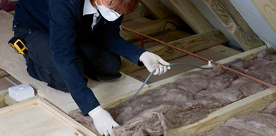 Person wearing gloves and a dust mask lifting an electric cable on top of loft insulation.