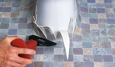 Sheet vinyl laid around the base of a toilet. Vertical cuts have been made in the vinyl around the toilet to allow it to be pushed around the toilet using a chisel.