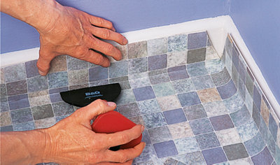 Using a bolster chisel to push vinyl flooring into the gap between a skirting board and floor.