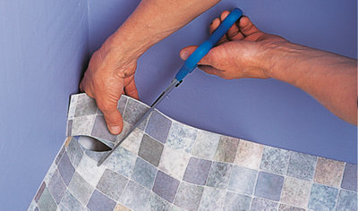 Using a pair of scissors to cut a triangular notch out of the corner of a vinyl sheet.