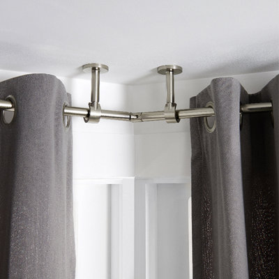 Curtain pole installed on an angle in a bay window, with two ceiling mounts on both sides of the angle and a join between the two sections of curtain pole.