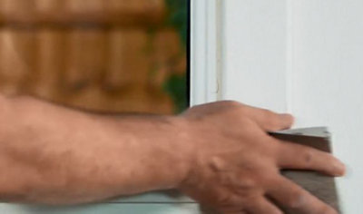 Person using a piece of sandpaper to sand down a wooden window frame.