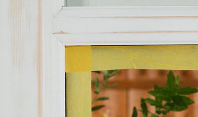 A wooden window frame with masking tape applied to the glass at the edges to protect it from paint.