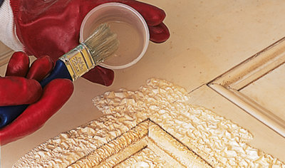 Person wearing gloves applying paint stripper to a door frame.