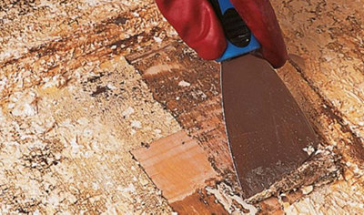 Person using a flat bladed scraper to remove the paint from an external door that has already been treated with paint stripper.