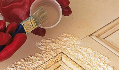 Person wearing gloves dipping a paintbrush into a pot of paint stripper. The paint on the door is bubbling as the paint stripper begins to work.