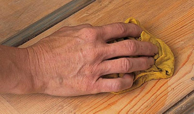 Person using a cloth to rub white spirit into a wooden front door to neutralise the surface.
