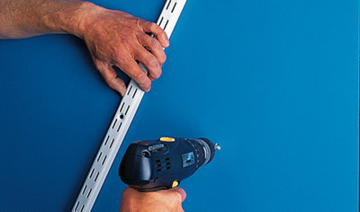 Using a drill to drill a hole in a wall ready for installation of a shelving upright.