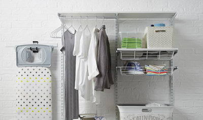Adjustable shelving mounted on a brick wall with three vertical uprights. A clothes rail, drawer and shelves are mounted on the uprights.