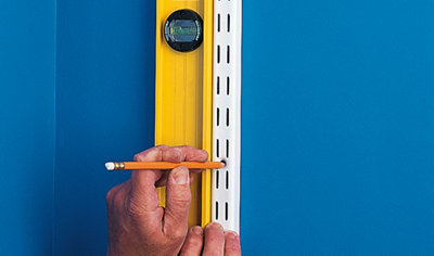 Person holding a spirit level against a shelving upright whilst marking the screw holes with a pencil.