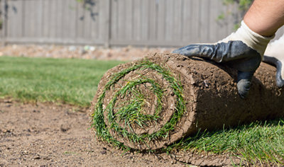 Person wearing gloves rolling out a roll of turf on top of soil.