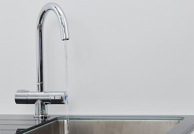 A newly installed chrome kitchen mixer tap running water into a kitchen sink.
