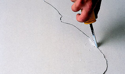 Person using a plasterboard jab saw to cut out a plasterboard repair patch based on a template that's been drawn in pencil.