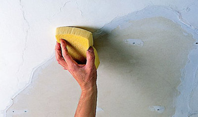 Person using a sponge to feather the edges of filler around a plasterboard repair patch on a ceiling.