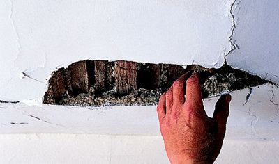 Person using their hand to pull down pieces of broken plaster from a ceiling to reveal wooden laths underneath.