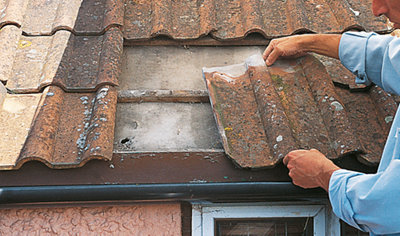 Person lifting a broken roof tile with two hands off a roof.