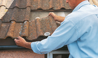 Person lifting up an existing roof tile to allow a new roof tile to slot underneath.