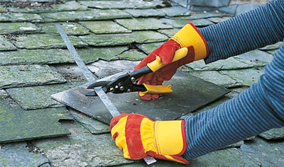 Person wearing gloves using a pair of tin snips to cut a metal strip on top of a slate roof.
