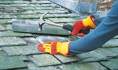 Person using a hammer to drive a nail through a metal strip to secure it to a slate roof.