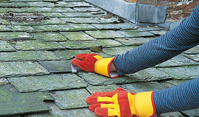Person bending a piece of metal that has been secured to a slate roof up and over the bottom of a new slate tile to secure it.