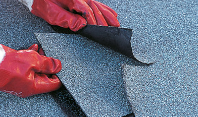 Person wearing gloves sliding a square patch of roof felt underneath a torn piece of roof felt.