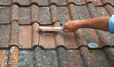 Person using a wire brush to clean the area around a cracked roof tile.