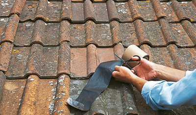 Person using a pair of scissors to cut a piece of flashing strip from a roll.