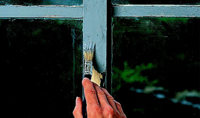Using a small paintbrush to apply rust remover to a metal window frame for restoration.