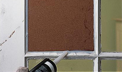 Using a sealant gun to apply sealant to the edges of a piece of timber placed in a window frame to weatherproof it.