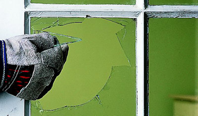 Person wearing rigger gloves carefully removing shards of glass from a broken window.