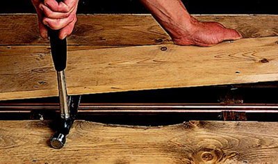 Using the claw end of a hammer to lift up a wooden floorboard.