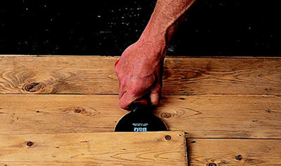 Person pushing a chisel underneath a wooden floorboard to lift it up.