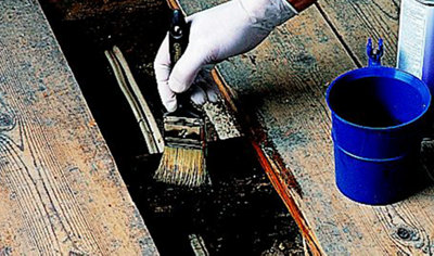 Person using a paintbrush to apply a woodworm treatment to the top of a wooden floorboard.