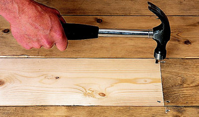 Person using a hammer and nail to secure a new floorboard to an existing floor.