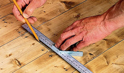Using a ruler and a pencil to mark the position of a joist on the top of a floorboard.